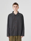 Top-half view of man wearing an Uskees charcoal-grey cotton overshirt indicating roomy, boxy fit with clear view of deep pockets on the chest and front.