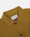 Close-up view of 3001 mustard-yellow, buttoned organic cotton overshirt from Uskees showing corozo buttons, branding label, collar and hanging loop.
