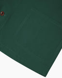 Front flat shot of green, buttoned organic cotton overshirt. Clear view of chest and hip pockets, corozo buttons and Uskees branding label.