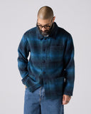 Model wearing peacock blue check, buttoned Pennine wool overshirt. Showing front and paired with jeans.