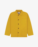 Front flat shot of yellow, buttoned organic cotton overshirt. Clear view of chest and hip pockets, corozo buttons and Uskees branding label.
