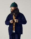 Male model wearing a deep indigo Uskees corduroy suit, green wool beanie, and glasses against a plain background.