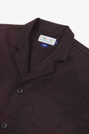 Close-up view of a dark plum-colored men's blazer, featuring a pointed collar, a chest pocket, and a visible USKEES brand label.