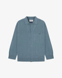 Flat front view of knitted organic cotton blue-grey collared cardigan with 3 patch pockets from Uskees. Clearly showing corozo buttons, two branding labels and 3 pockets on the front.