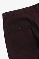 Close-up reverse view of Uskees dark plum colour pants showing the waistband with waist adjuster buttons, belt loops, and a buttoned flap pocket.