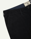 Close-up front view of left front pocket, belt loops, triple stitching, branding label and contrasting lining. Also a closer view of the organic, 11 wale corduroy in midnight blue.