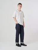 Full-length front view of male model wearing Uskees raw orta denim workwear pants in dark indigo paired with off-white shirt.
