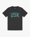 Full flat view of faded black organic cotton signature T-shirt for men, showing the varsity inspired 'USK' logo on the chest and the Uskees branding labels on the neck and hem.