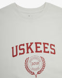 Neckline close-up of white organic cotton T-shirt, with focus on the neck tape reinforcement and Uskees Racquet Club brand graphics in white.