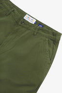 Close up of waist area of twill workwear pants in coriander-green. Clear view of front pocket, Corozo button fastening, Uskees branding label and organic cotton twill weave.