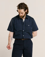 Male model wearing an Uskees navy short-sleeve shirt and pants on a beige background.